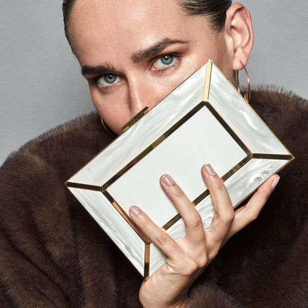 YLIANA YEPEZ Minaudiere. Rectangular clutch with gold frame and beige interior on a white background