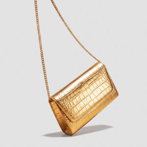 A metallic gold crocodile-embossed leather clutch bag with a matching gold chain strap, shown against a solid light gray background.