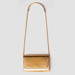 A gold crocodile-embossed leather crossbody bag with a matching gold chain strap and top handle, shown against a light gray background.