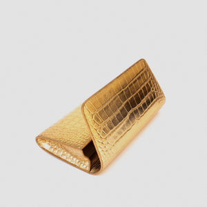 A gold-toned clutch wallet with a crocodile-embossed texture, shown closed on a light gray background.