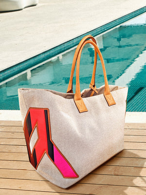 Beige tote bag with colorful design on a wooden deck by a pool