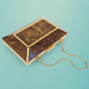 Gold clutch with a chain on a light blue background